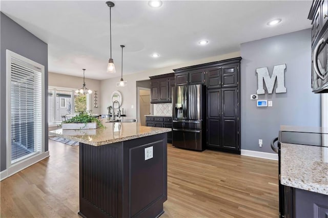 kitchen featuring light stone countertops, stainless steel appliances, light hardwood / wood-style flooring, decorative light fixtures, and a center island with sink