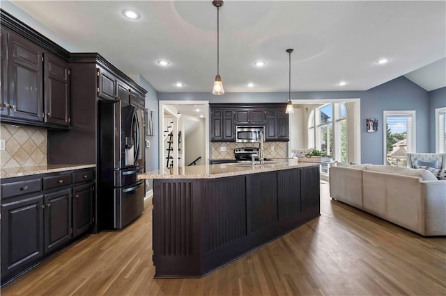 kitchen with tasteful backsplash, hanging light fixtures, stainless steel appliances, and light hardwood / wood-style flooring