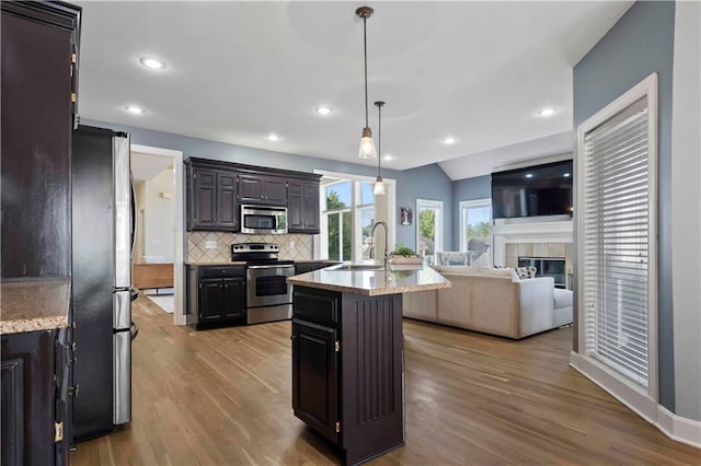 kitchen with pendant lighting, a center island with sink, sink, light wood-type flooring, and stainless steel appliances