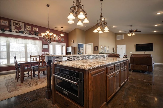 kitchen with ceiling fan with notable chandelier, a center island, hanging light fixtures, oven, and light stone counters