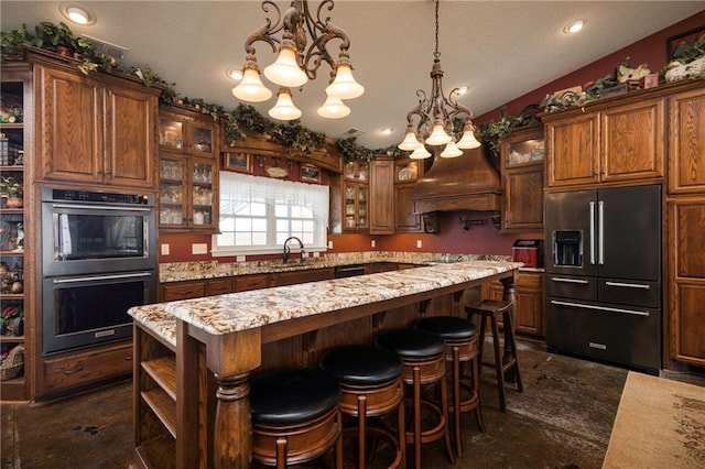 kitchen featuring double wall oven, high end fridge, a kitchen island, light stone counters, and sink