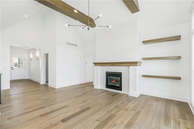 unfurnished living room with baseboards, beamed ceiling, light wood-type flooring, a fireplace, and a notable chandelier