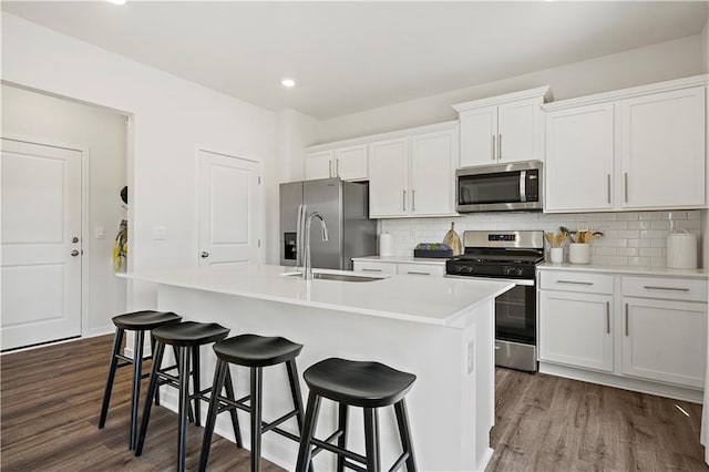 kitchen featuring appliances with stainless steel finishes, white cabinetry, dark wood-type flooring, and an island with sink