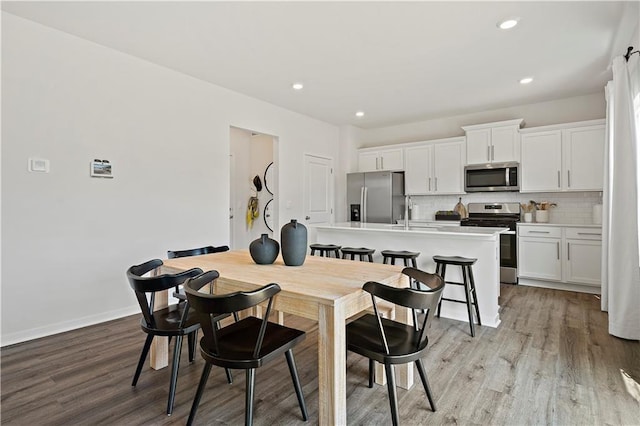 kitchen featuring backsplash, an island with sink, light hardwood / wood-style floors, white cabinets, and appliances with stainless steel finishes