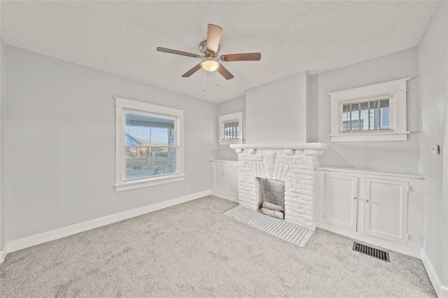 unfurnished living room with ceiling fan, light colored carpet, a stone fireplace, and a textured ceiling