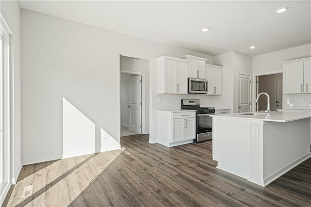 kitchen with a kitchen island with sink, sink, dark hardwood / wood-style flooring, white cabinetry, and stainless steel appliances