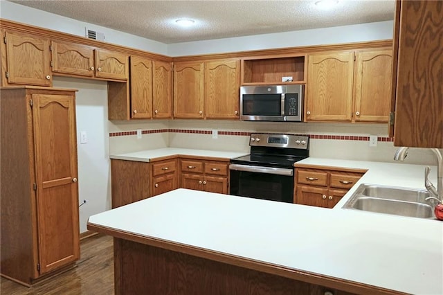 kitchen with sink, dark wood-type flooring, stainless steel appliances, kitchen peninsula, and a textured ceiling