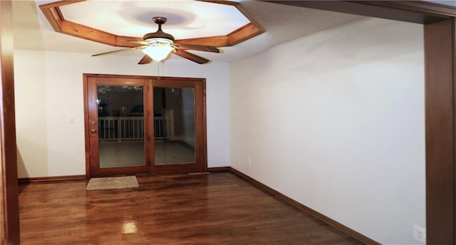 unfurnished room featuring a raised ceiling, ceiling fan, and dark hardwood / wood-style floors