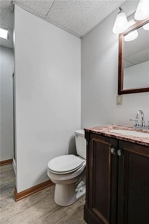 bathroom featuring a drop ceiling, wood-type flooring, toilet, vanity, and a shower with shower door