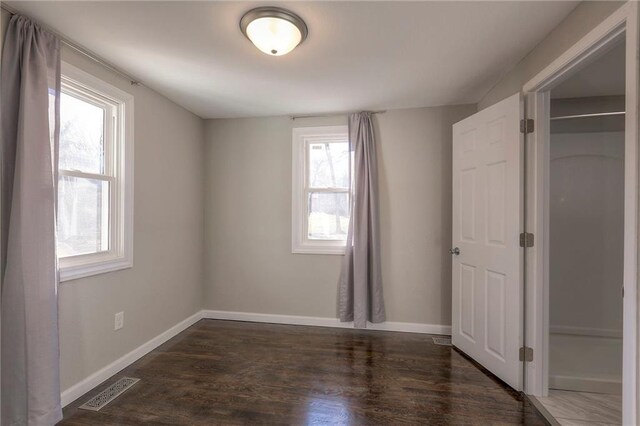 unfurnished bedroom featuring multiple windows, a closet, and dark hardwood / wood-style flooring