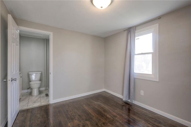 unfurnished bedroom featuring ensuite bathroom and dark hardwood / wood-style floors