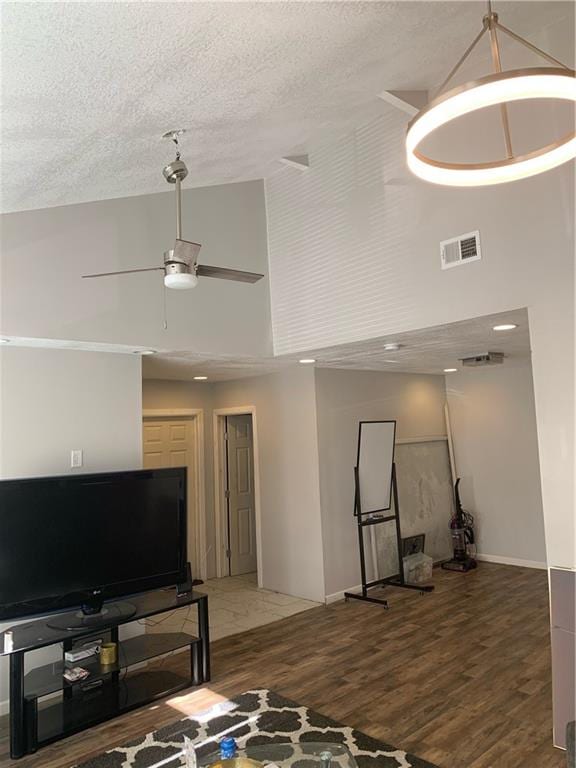 living room featuring ceiling fan, dark hardwood / wood-style flooring, a textured ceiling, and a high ceiling