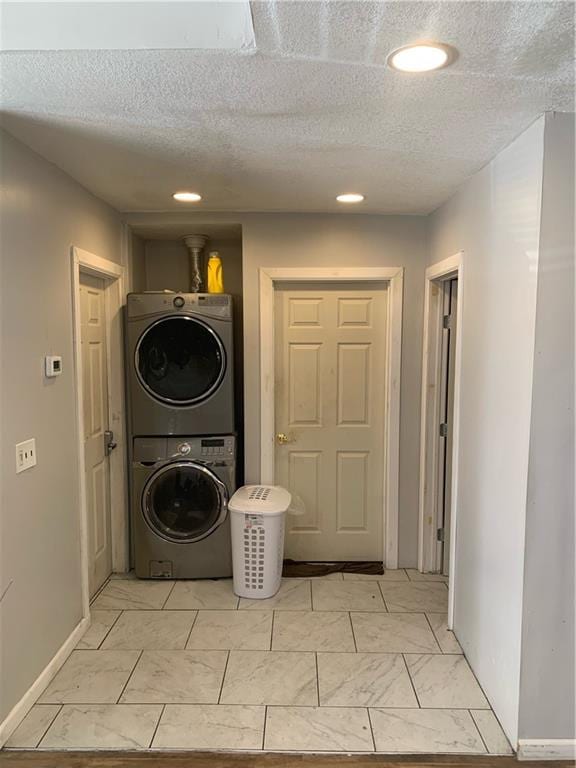 clothes washing area with a textured ceiling and stacked washer / dryer