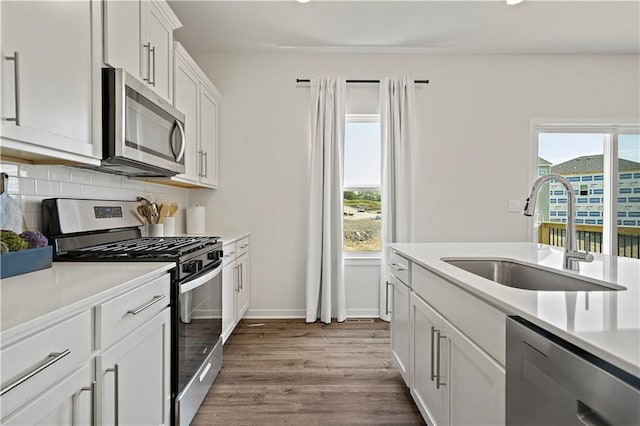 kitchen with sink, appliances with stainless steel finishes, decorative backsplash, white cabinets, and light wood-type flooring