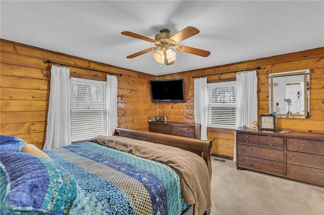 carpeted bedroom with multiple windows, wooden walls, and ceiling fan