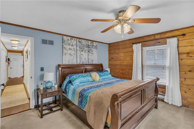 carpeted bedroom featuring wood walls, crown molding, ceiling fan, and a baseboard heating unit