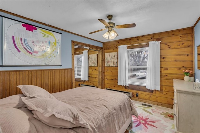 bedroom featuring ceiling fan, a baseboard radiator, wooden walls, and multiple windows