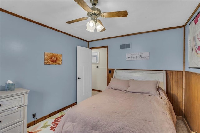 carpeted bedroom with ceiling fan, wooden walls, and ornamental molding