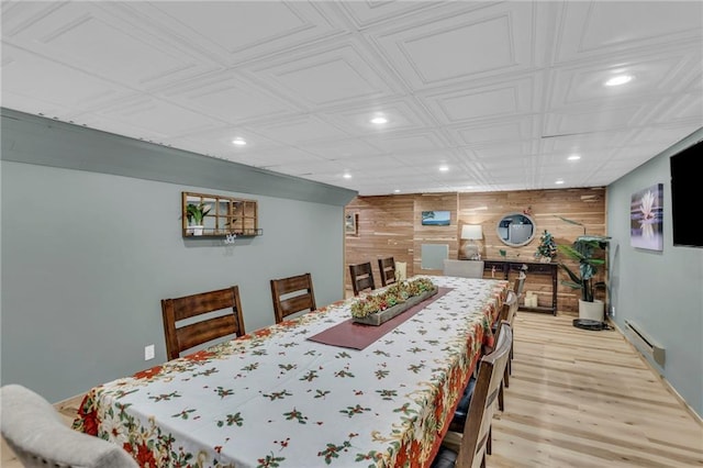 dining room with a baseboard radiator, light hardwood / wood-style flooring, and wooden walls