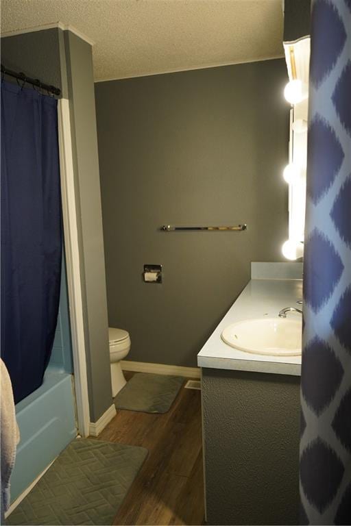 full bathroom with hardwood / wood-style floors, a textured ceiling, toilet, shower / bath combo with shower curtain, and vanity