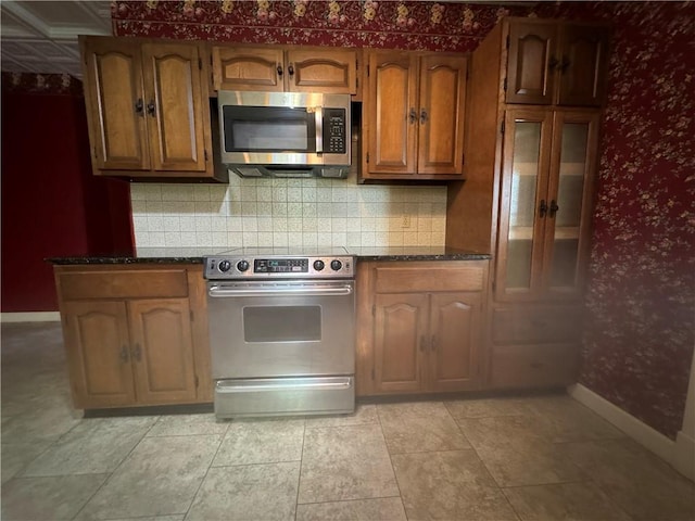 kitchen featuring appliances with stainless steel finishes, backsplash, light tile patterned floors, and dark stone countertops