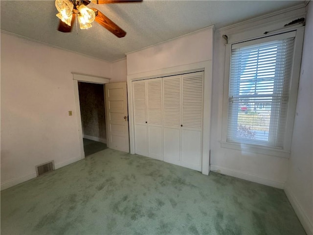 unfurnished bedroom featuring carpet, ornamental molding, a textured ceiling, ceiling fan, and a closet