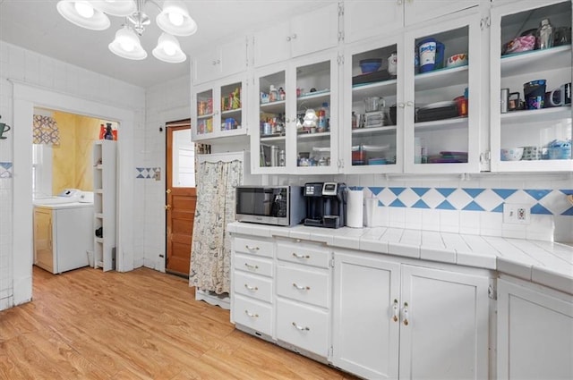 kitchen with backsplash, tile countertops, washer / dryer, light hardwood / wood-style floors, and white cabinetry