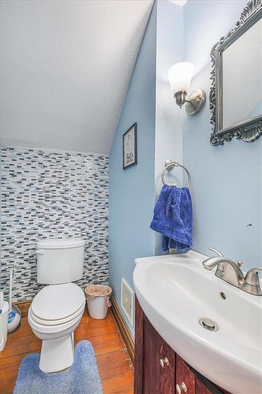 bathroom with tile walls, wood-type flooring, lofted ceiling, and toilet