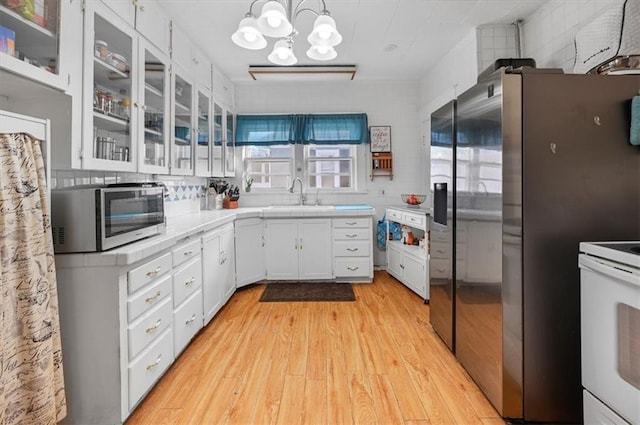 kitchen featuring white cabinetry, glass insert cabinets, a sink, appliances with stainless steel finishes, and light wood finished floors