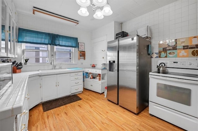 kitchen featuring a sink, light wood-style floors, stainless steel refrigerator with ice dispenser, tile countertops, and white electric stove