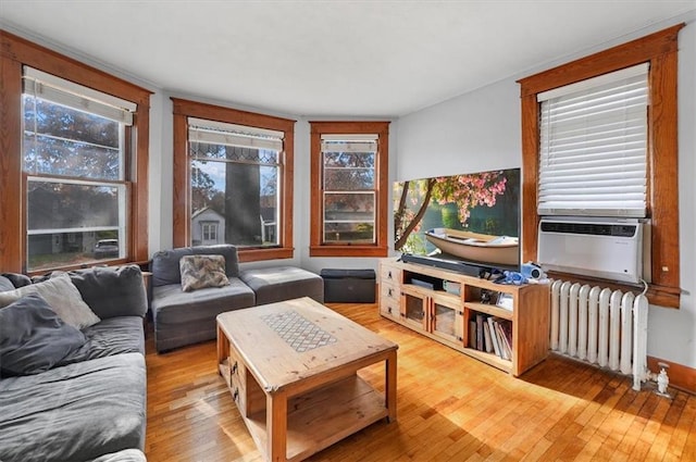 living area with radiator heating unit, cooling unit, and light wood-style flooring