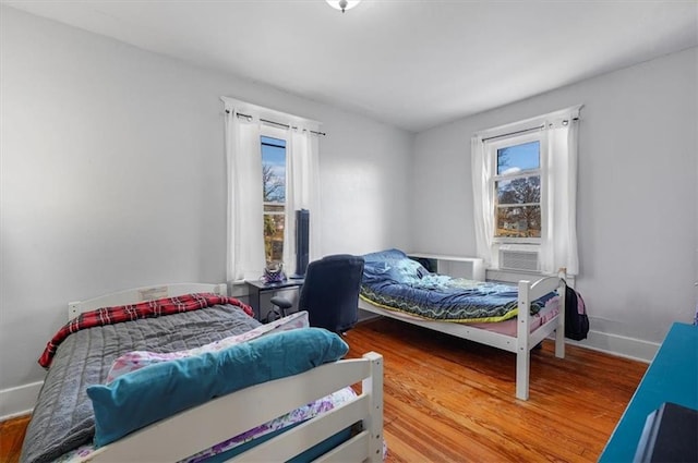 bedroom with cooling unit, multiple windows, wood finished floors, and baseboards