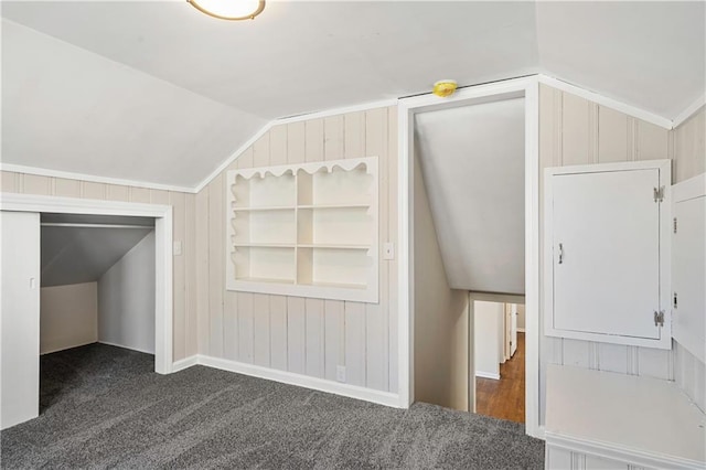 additional living space with vaulted ceiling, dark carpet, and wood walls