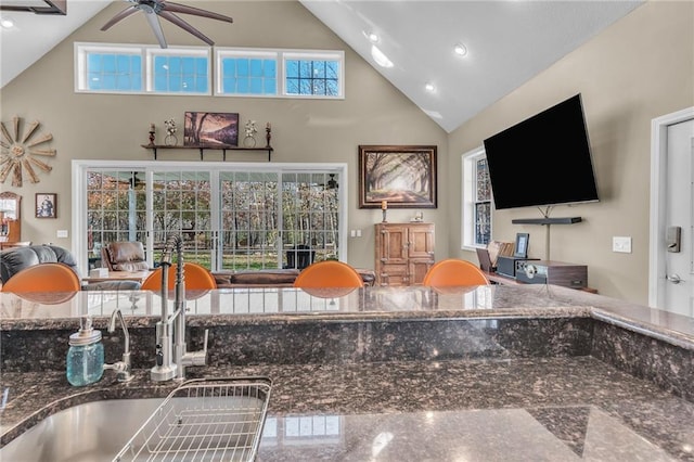 kitchen featuring dark stone countertops, ceiling fan, high vaulted ceiling, and a healthy amount of sunlight