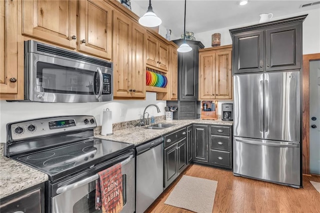 kitchen featuring hanging light fixtures, sink, light hardwood / wood-style flooring, light stone countertops, and appliances with stainless steel finishes