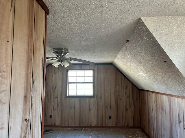 additional living space featuring ceiling fan, wood walls, lofted ceiling, and a textured ceiling