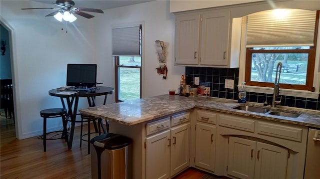 kitchen featuring backsplash, sink, ceiling fan, light wood-type flooring, and kitchen peninsula