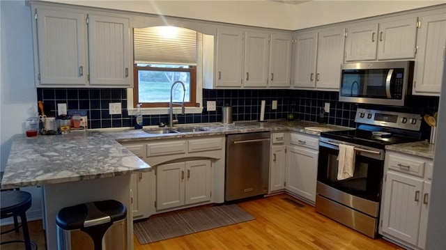 kitchen featuring sink, light hardwood / wood-style flooring, appliances with stainless steel finishes, tasteful backsplash, and kitchen peninsula