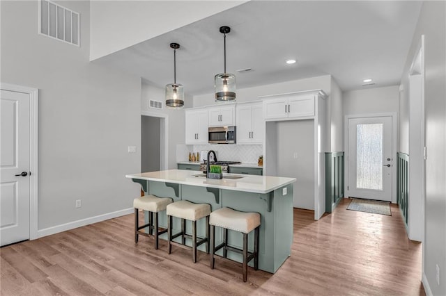 kitchen with a breakfast bar, white cabinetry, an island with sink, pendant lighting, and stainless steel appliances