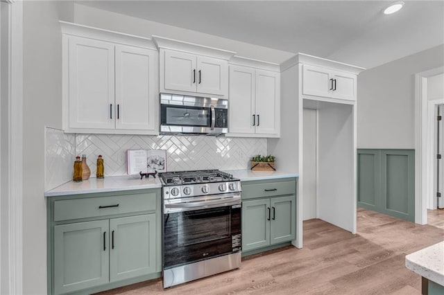 kitchen with green cabinets, stainless steel appliances, tasteful backsplash, white cabinets, and light wood-type flooring