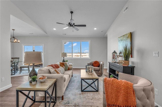 living room with ceiling fan with notable chandelier and hardwood / wood-style floors