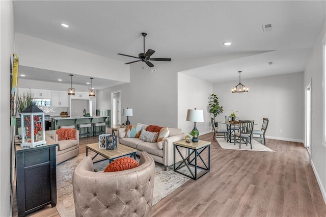 living room featuring ceiling fan with notable chandelier, light hardwood / wood-style flooring, a wealth of natural light, and vaulted ceiling