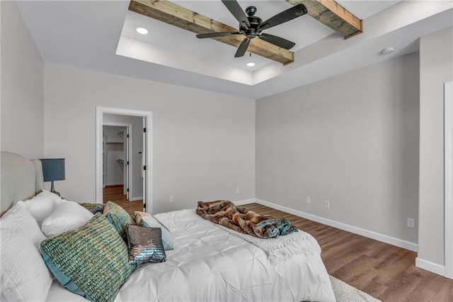 bedroom featuring hardwood / wood-style flooring, a walk in closet, ceiling fan, a raised ceiling, and beam ceiling