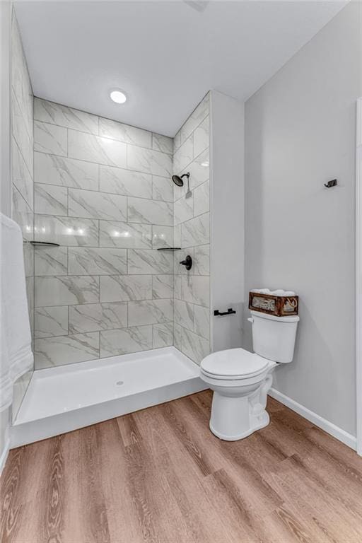 bathroom with hardwood / wood-style flooring, tiled shower, and toilet