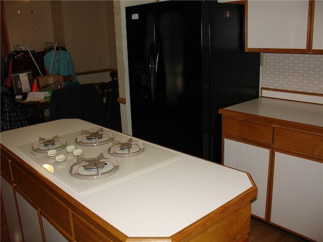 kitchen with black refrigerator with ice dispenser, a kitchen island, wood-type flooring, and white gas cooktop