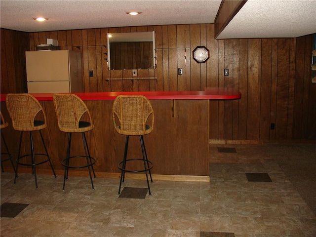 bar featuring a textured ceiling, white fridge, and wood walls