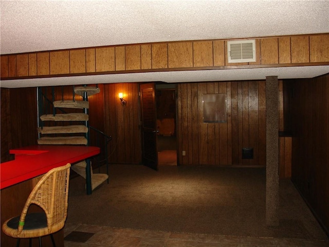 basement featuring dark carpet, a textured ceiling, and wooden walls