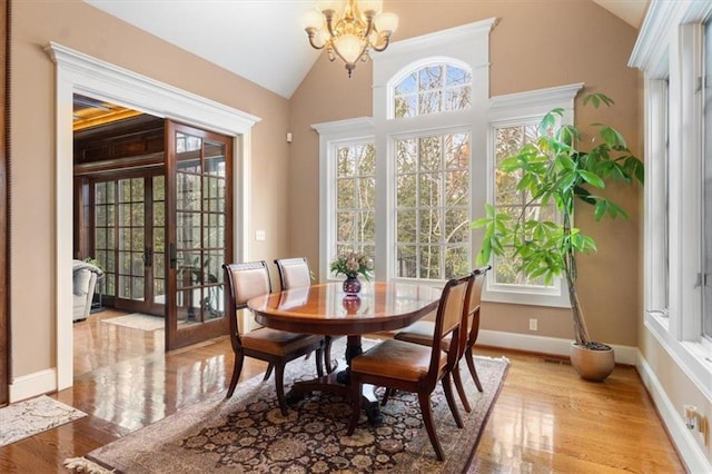 dining space with a chandelier, french doors, light hardwood / wood-style floors, and lofted ceiling