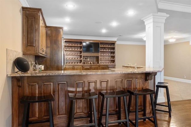 bar with light stone countertops, light tile patterned floors, ornate columns, and crown molding