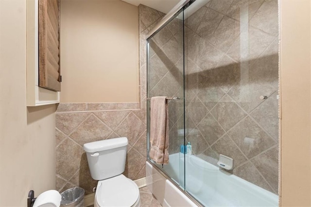 bathroom featuring shower / bath combination with glass door, tile walls, and toilet